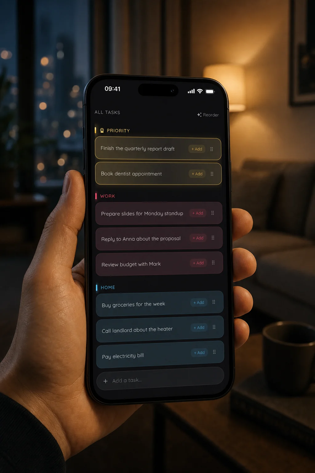 A hand holding an iPhone showing Podomodo tasks sorted into Priority, Work and Home, in a living room at night